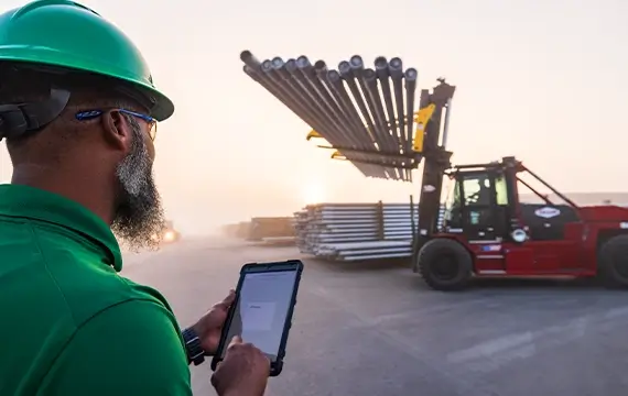 A Workstrings worker checking off safey information on his tablet while a forklift transports drill pipes