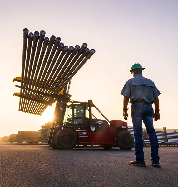 A Workstrings worker looking up at drill strings being carried by a forklift at dawn