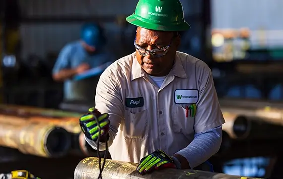 A Workstrings worker taking readings from a small handheld device while looking at drill pipes
