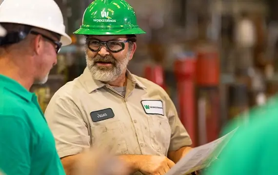 A Workstrings worker pointing out specs on a piece of paper to a coworker in a warehouse