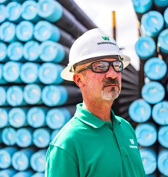 A close up of a Workstrings worker in a green shirt and safety glasses looking off into the distance
