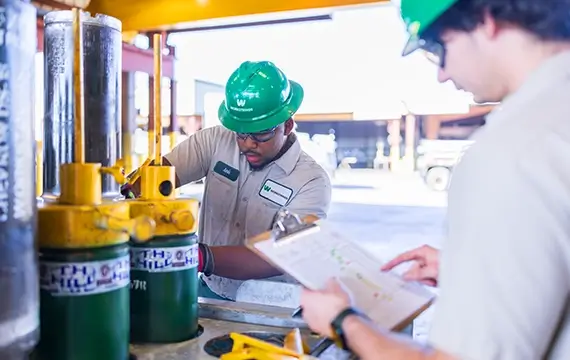 Workstrings warehouse worker looking at drill components while another goes over a checklist on his clipboard 