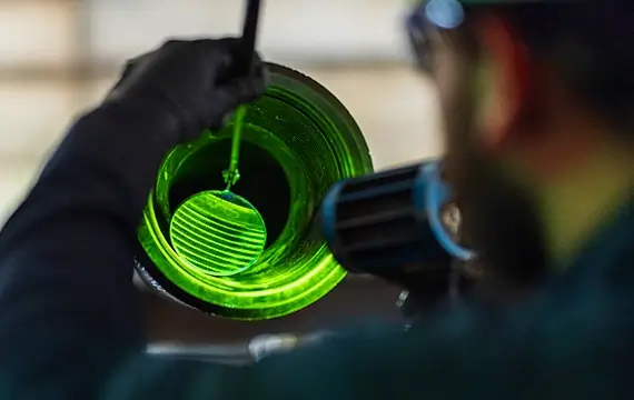 A Workstrings worker examining the interior of a drill string with a mirror and green light