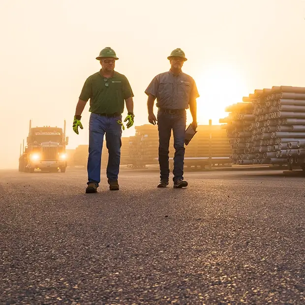 Two Workstrings workers walking at dawn with an eighteen-wheeler driving toward them in the background