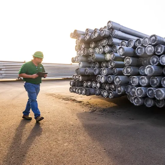 A Workstrings worker walking by a huge stack of downhole tubulars, taking inventory